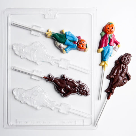 A pumpkin scarecrow lollipop mold shown along side two finished pumpkin scarecrow lollipops painted in bright colors. The plastic chocolate mold and finished chocolate lollipops are displayed on a white background.
