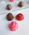 Chocolate rose candies in brown, red, and pink on a white surface with plastic mold in the background