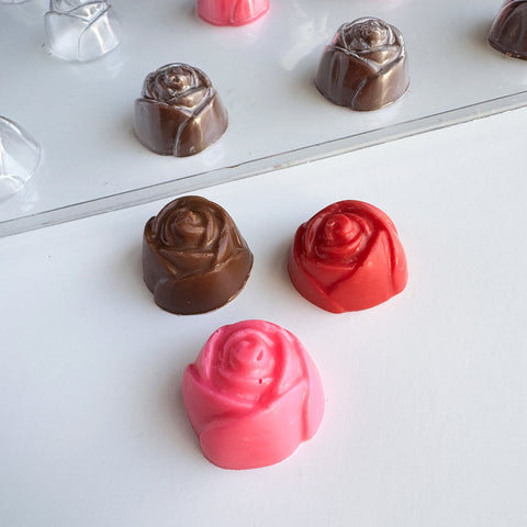 Chocolate rose candies in brown, red, and pink on a white surface with plastic mold in the background