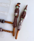 Two Halloween themed chocolate witch pretzel rods along side the spooky witch plastic pretzel rod mold used to make them