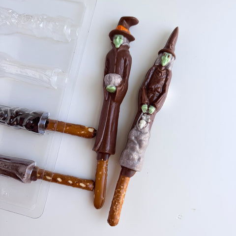 Two Halloween themed chocolate witch pretzel rods along side the spooky witch plastic pretzel rod mold used to make them