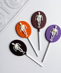 4 oval skeleton lollipop chocolates next to the plastic candy mold used to make them on a white background