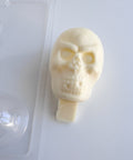 Plastic skull candy mold next to a finished white chocolate 3d skull that has a chocolate base at the bottom to insert into a cake and use as a topper, all sitting on a white back drop.