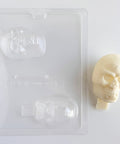 Plastic skull candy mold next to a finished white chocolate 3d skull that has a chocolate base at the bottom to insert into a cake and use as a topper.