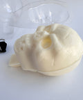 Plastic skull candy mold next to a finished white chocolate 3d skull that has a chocolate base at the bottom to insert into a cake and use as a topper.
Binder clips that were used for clamping the mold together are shown on the left.