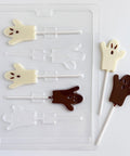 A clear plastic Halloween ghost lollipop candy mold shown with five finished ghost-shaped lollipops on a white background: two in milk chocolate and three in white chocolate, each with small eyes and mouth details.