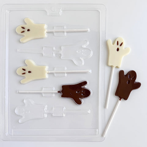A clear plastic Halloween ghost lollipop candy mold shown with five finished ghost-shaped lollipops on a white background: two in milk chocolate and three in white chocolate, each with small eyes and mouth details.
