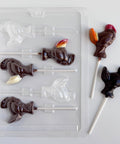 plastic turkey lollipop candy mold shown with two finished turkey chocolate lollipops, one made from dark chocolate and the other from milk chocolate with details painted in red, orange, and yellow.