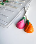 chocolate lollipops in pink and orange shaped like little roses next to plastic candy mold