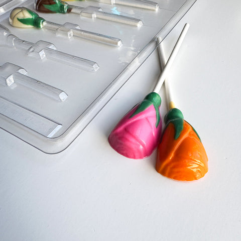 chocolate lollipops in pink and orange shaped like little roses next to plastic candy mold