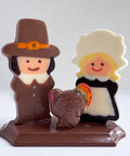 A chocolate centerpiece for thanksgiving shaped like two pimgrims and a turkey sitting on a chocolate base
