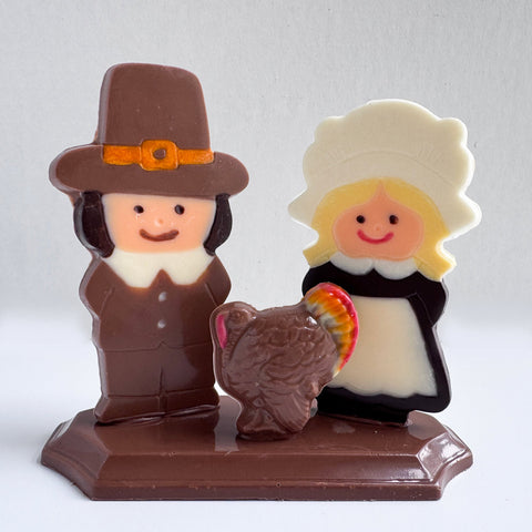 A chocolate centerpiece for thanksgiving shaped like two pimgrims and a turkey sitting on a chocolate base