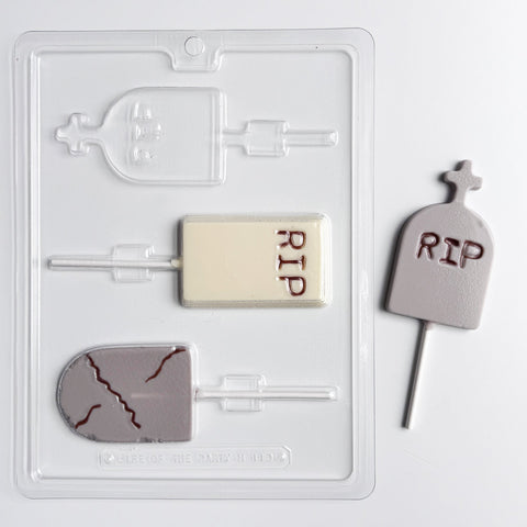 A Halloween-themed chocolate mold on a white background. Featuring tombstone shaped lollipops in three different designs., one rectangle with straight edges and RIP molded into the center, one rounded classic grave stone shape with a cracked look, and one rounded with a cross shape protruding off the top and RIP molded into the center. Shown with a finished lollipop to the right.