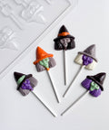 Five Halloween-themed witch head chocolate lollipops with witch hats and faces, arranged on a white surface next to a clear plastic candy mold.