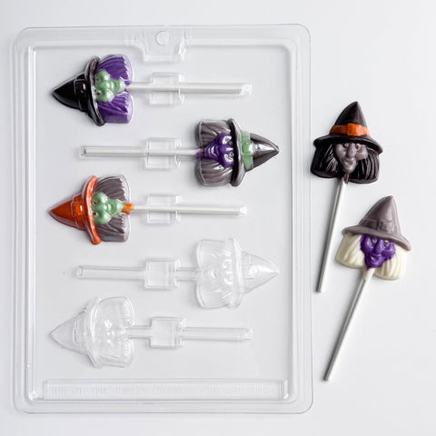 Witch face chocolate lollipops with three inside of the plastic candy mold used to make them and two sitting outside of the mold to the right. The lollipops are made with an assortment of colored chocolate.